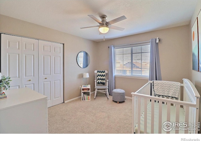 carpeted bedroom with a crib, baseboards, a closet, and a textured ceiling