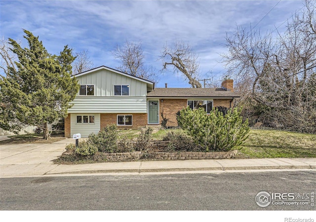 tri-level home with brick siding, board and batten siding, concrete driveway, and a chimney