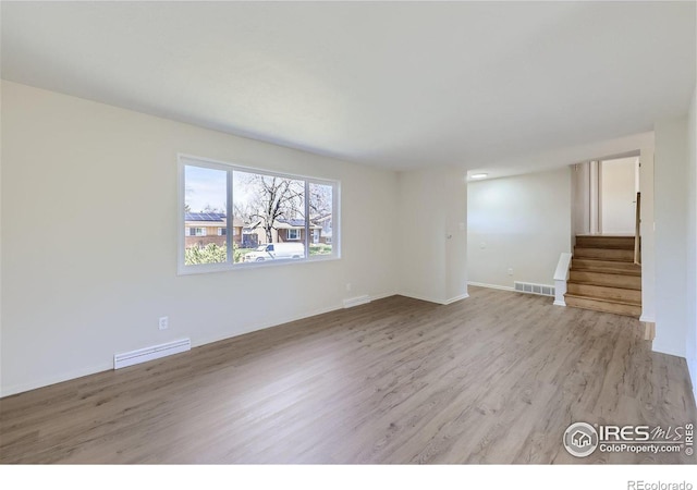 empty room featuring light wood finished floors, visible vents, stairway, and baseboards