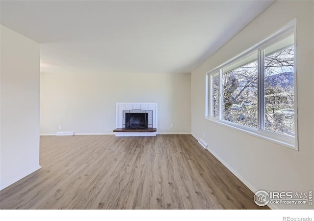 unfurnished living room with visible vents, baseboards, a brick fireplace, and wood finished floors