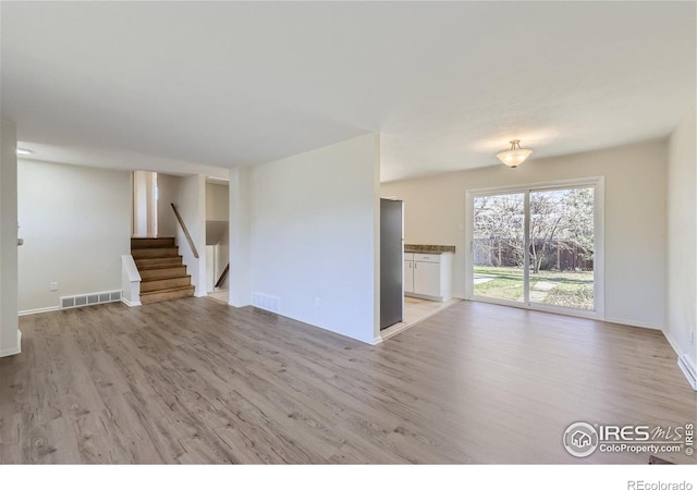 unfurnished living room featuring stairs, baseboards, visible vents, and light wood finished floors