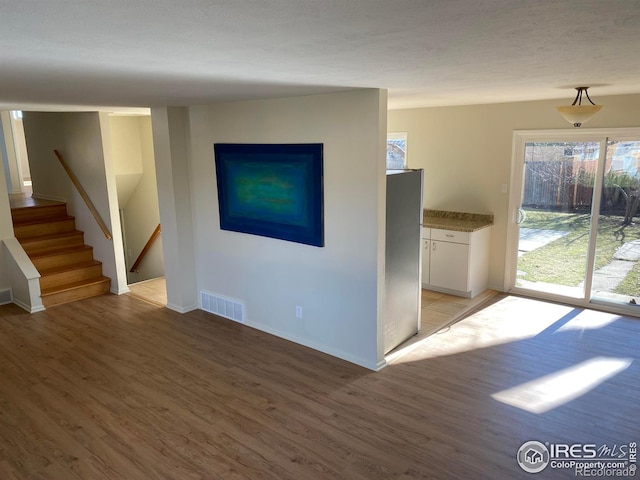 unfurnished living room featuring stairway, visible vents, and light wood finished floors