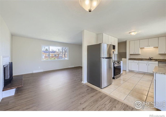 kitchen featuring light wood finished floors, open floor plan, white cabinets, stainless steel appliances, and a sink