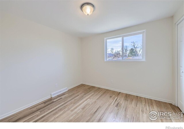 spare room featuring a baseboard heating unit, baseboards, visible vents, and wood finished floors