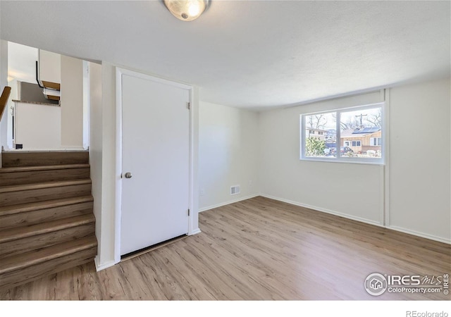 empty room with stairway, light wood-style floors, visible vents, and baseboards