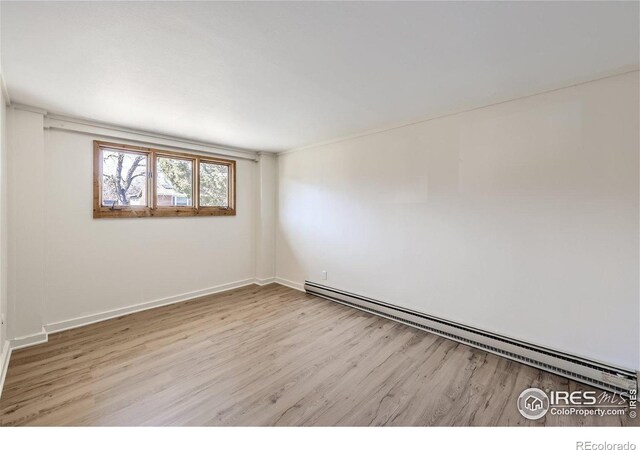 unfurnished room featuring baseboard heating, baseboards, and wood finished floors