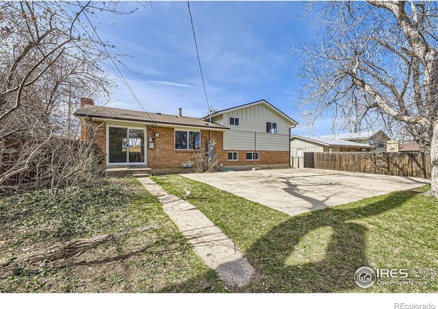 back of property with a lawn, driveway, fence, brick siding, and a chimney