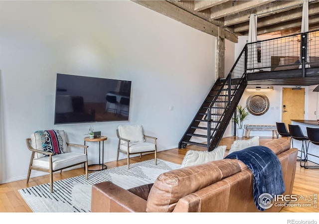 living room featuring beamed ceiling, wood finished floors, baseboards, a towering ceiling, and stairs