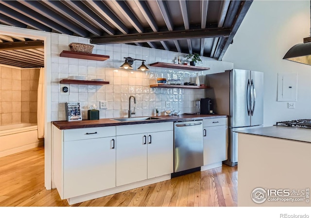 kitchen with light wood-type flooring, open shelves, stainless steel appliances, a sink, and tasteful backsplash