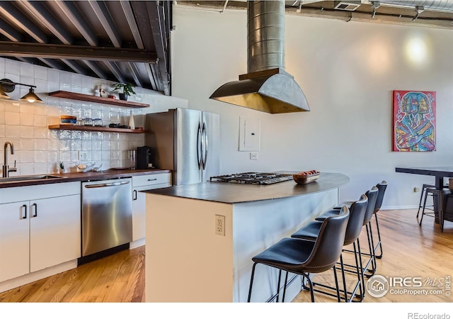 kitchen featuring light wood-style flooring, a sink, decorative backsplash, white cabinets, and appliances with stainless steel finishes