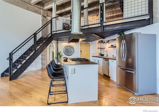 kitchen with stainless steel appliances, white cabinets, light wood-style floors, a towering ceiling, and a kitchen breakfast bar