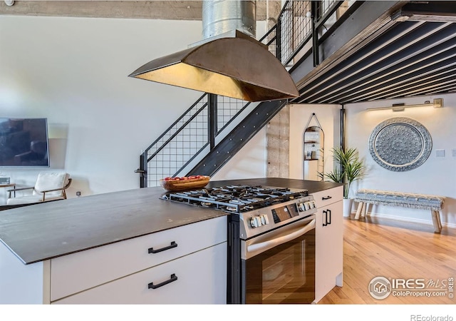 kitchen with light wood-type flooring, dark countertops, white cabinetry, baseboards, and stainless steel range with gas stovetop