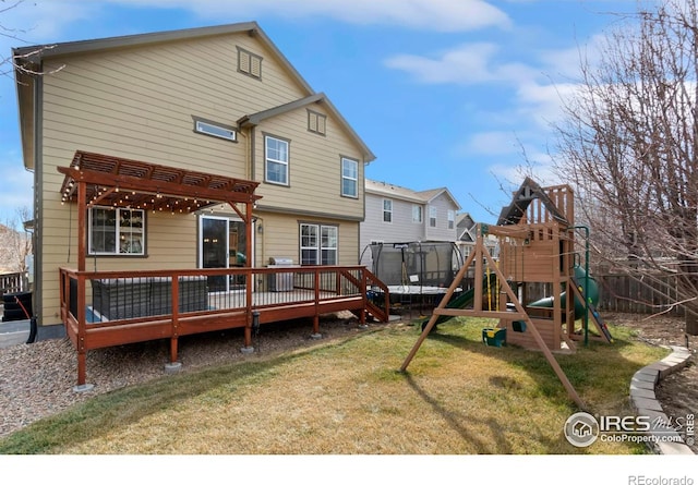 rear view of property featuring a playground, a trampoline, a lawn, a deck, and a pergola