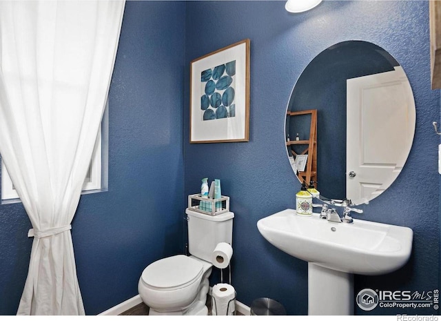 bathroom featuring toilet, a textured wall, baseboards, and a sink