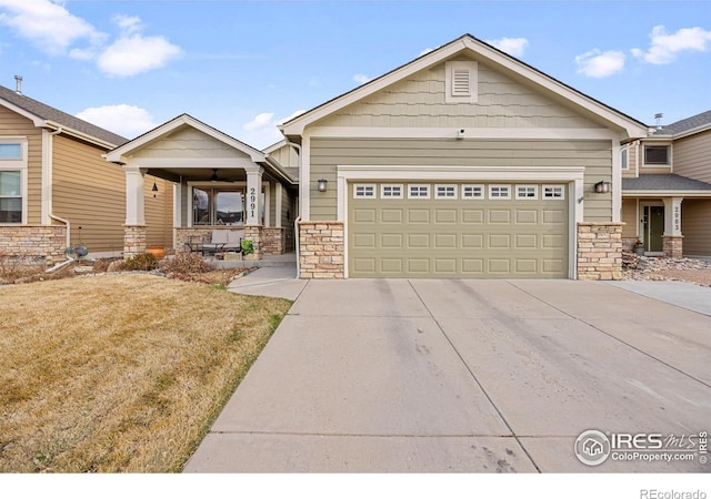 view of front of house with a front yard, covered porch, driveway, stone siding, and an attached garage