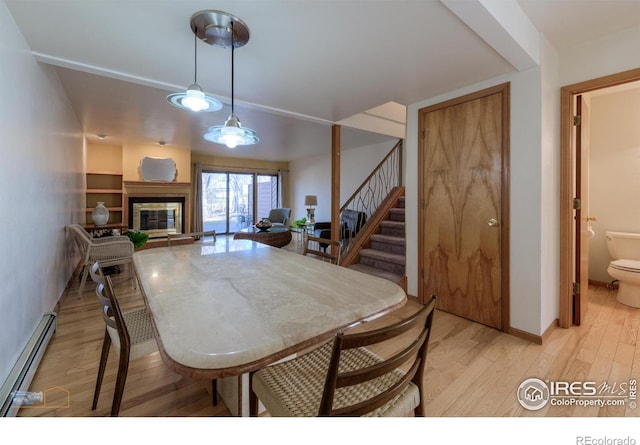 dining area featuring baseboards, a baseboard radiator, stairs, light wood-style floors, and a glass covered fireplace