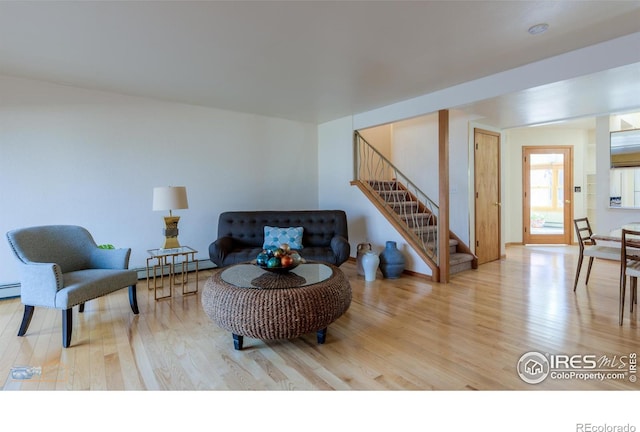 living area with a baseboard radiator, wood finished floors, and stairway