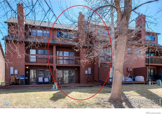 back of house with a wooden deck, a balcony, a lawn, and a chimney