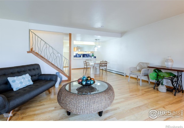 living room with stairs, a baseboard heating unit, baseboards, and wood finished floors