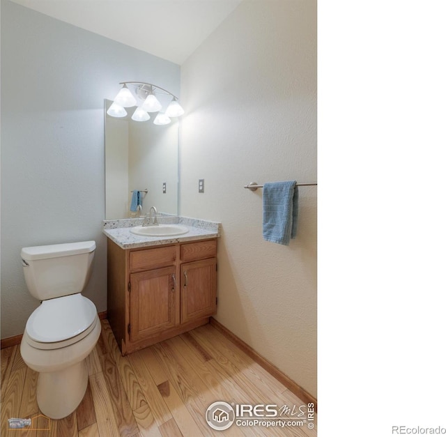 half bath with vanity, toilet, wood finished floors, and baseboards