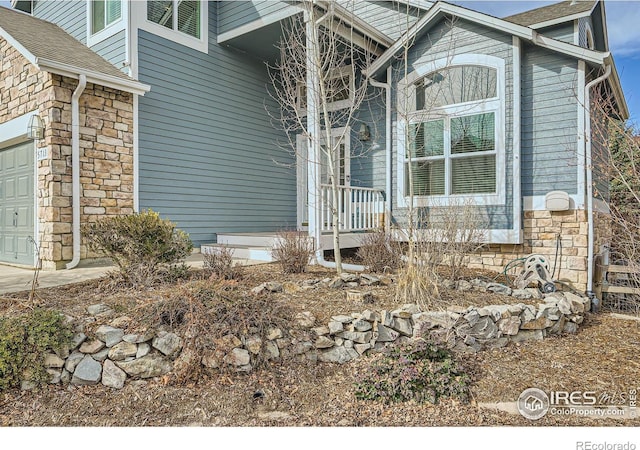 entrance to property with a garage, stone siding, and a shingled roof