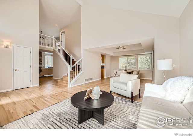 living area with a high ceiling, stairway, wood finished floors, and visible vents