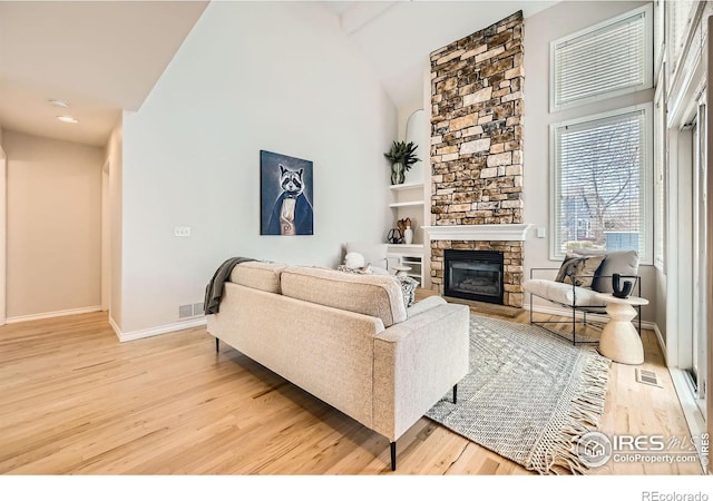 living room featuring a stone fireplace, visible vents, light wood-type flooring, and high vaulted ceiling