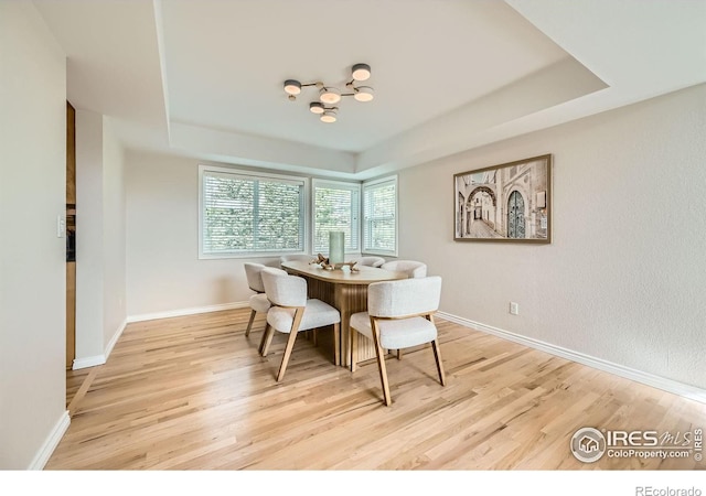 dining space featuring light wood-type flooring, baseboards, and a raised ceiling