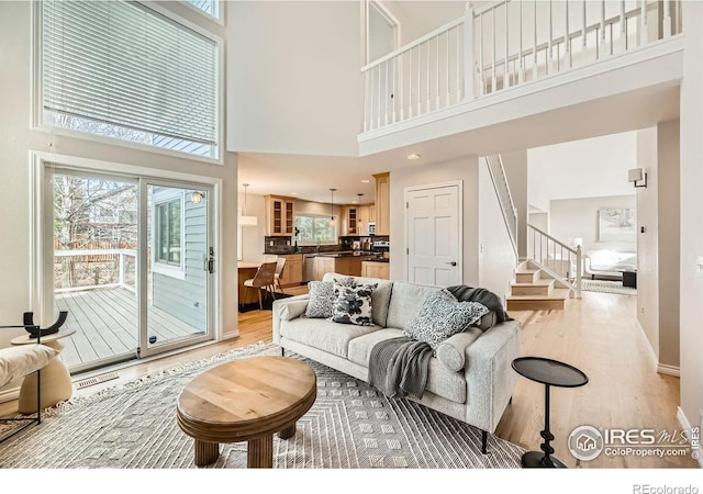 living room with visible vents, baseboards, stairway, light wood-style flooring, and a towering ceiling