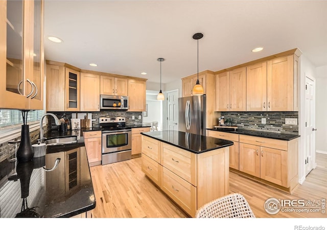 kitchen featuring light wood-style flooring, light brown cabinetry, a sink, appliances with stainless steel finishes, and glass insert cabinets