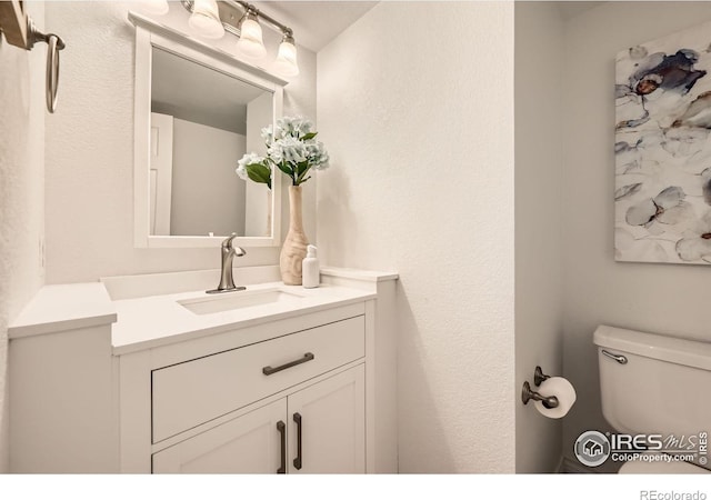 half bath featuring vanity, toilet, and a textured wall