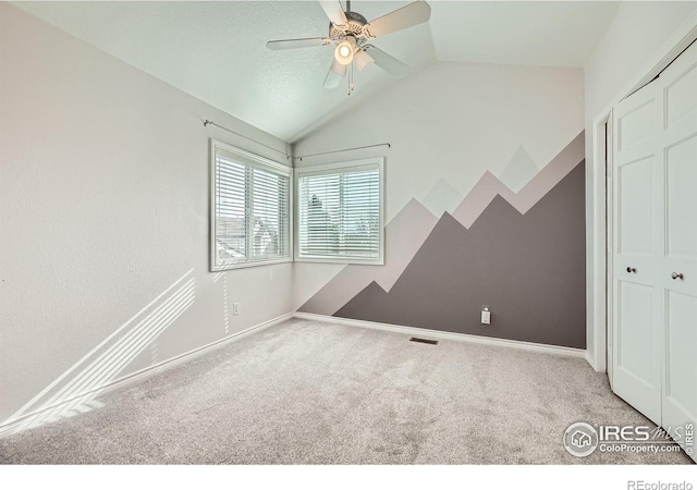 carpeted spare room featuring visible vents, ceiling fan, baseboards, and lofted ceiling