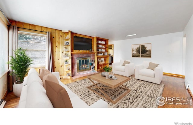 living room with wooden walls, a brick fireplace, baseboards, and wood finished floors