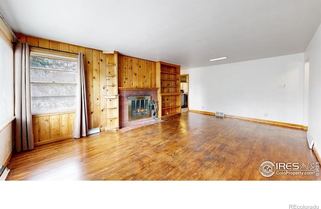 unfurnished living room with a fireplace, wood finished floors, visible vents, and wood walls