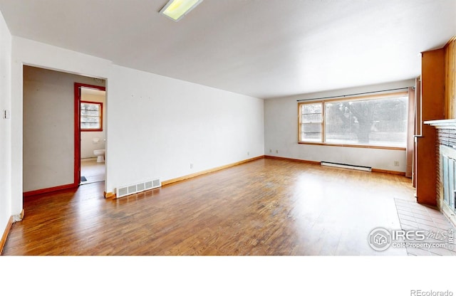 spare room featuring baseboards, visible vents, light wood finished floors, a baseboard radiator, and a fireplace