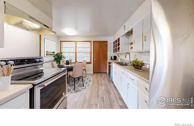 kitchen featuring under cabinet range hood, a sink, white cabinetry, stainless steel appliances, and decorative backsplash