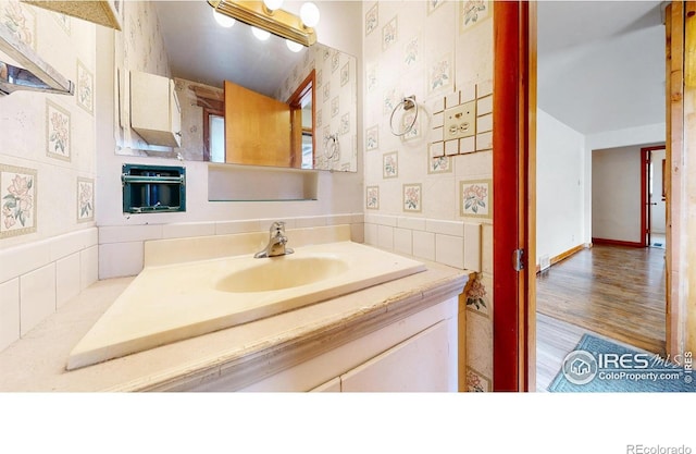 bathroom featuring baseboards, wood finished floors, vanity, and wallpapered walls