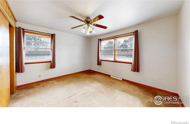 carpeted spare room with visible vents, a healthy amount of sunlight, a ceiling fan, and baseboards