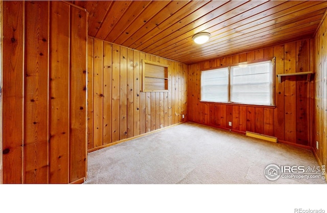 carpeted spare room featuring a baseboard heating unit, wooden ceiling, wooden walls, and baseboards