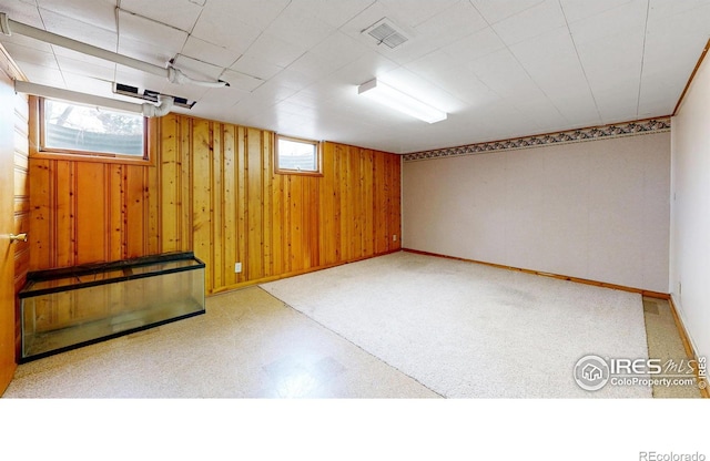 basement with tile patterned floors, visible vents, wood walls, and baseboards