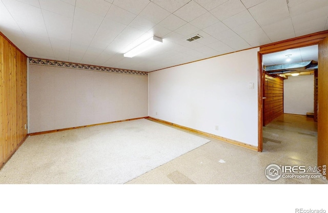 empty room with baseboards, visible vents, wood walls, and carpet floors