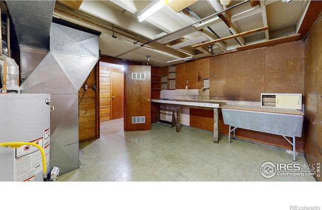 unfinished below grade area featuring tile patterned floors, visible vents, a workshop area, and wooden walls