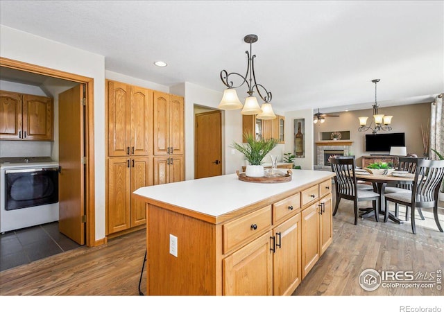 kitchen featuring washer / dryer, a brick fireplace, wood finished floors, and a kitchen island