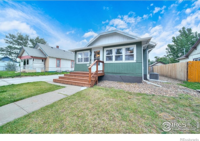 bungalow with board and batten siding, central AC, a front yard, and fence