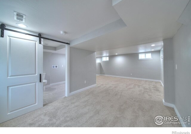 basement featuring visible vents, baseboards, a barn door, and carpet floors