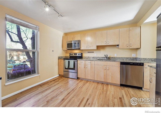 kitchen with light brown cabinets, a sink, stainless steel appliances, light wood finished floors, and baseboards