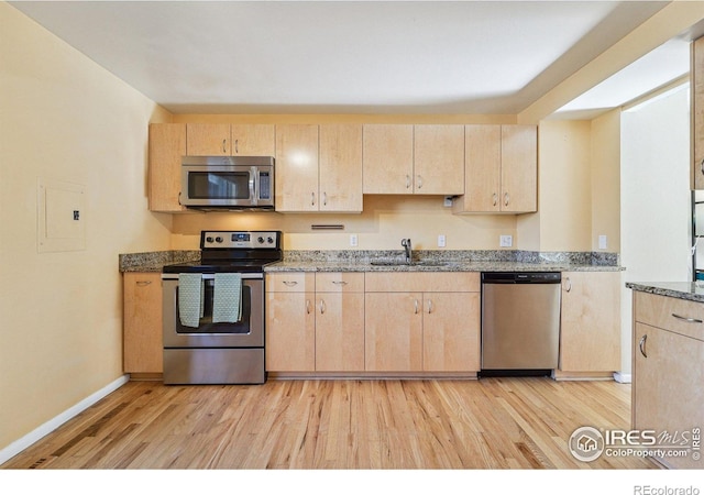 kitchen featuring stone countertops, a sink, light brown cabinetry, stainless steel appliances, and light wood-type flooring