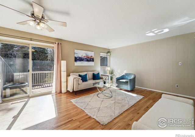 living room featuring ceiling fan, visible vents, baseboards, and wood finished floors