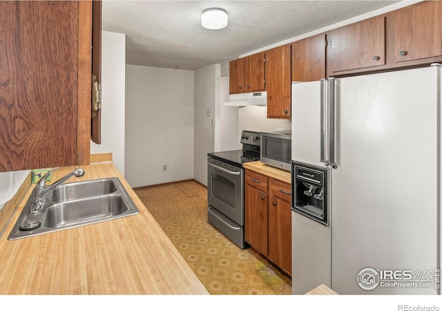 kitchen with a sink, under cabinet range hood, a textured ceiling, appliances with stainless steel finishes, and light floors