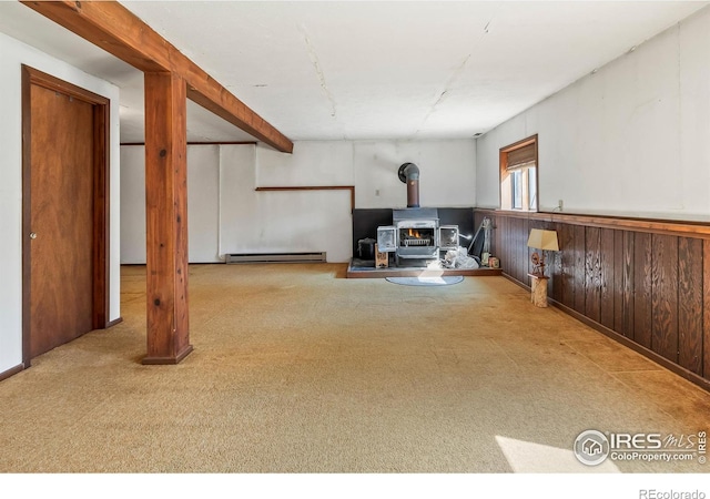 basement featuring a baseboard heating unit, a wood stove, carpet, and wainscoting